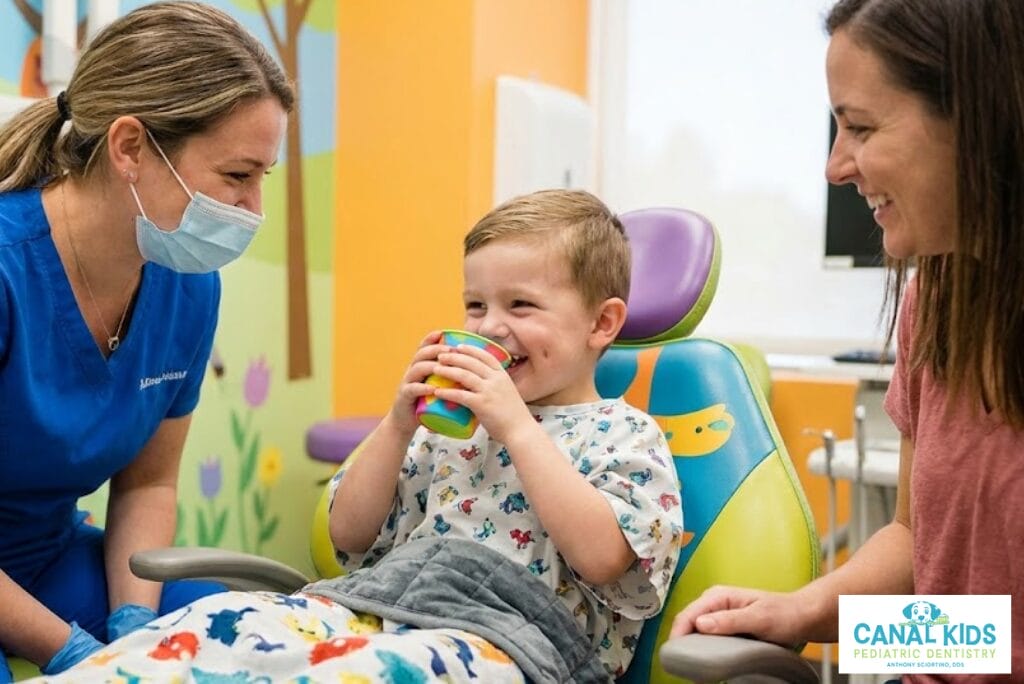 Child drinking oral sedation while smiling with dentist and mother during dental visit